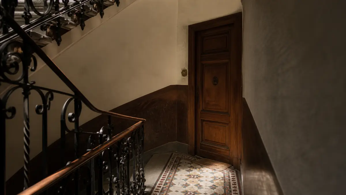 Rellano de una finca antigua de Gràcia, con suelo de mosaico hidráulico y una puerta de madera sin placa.